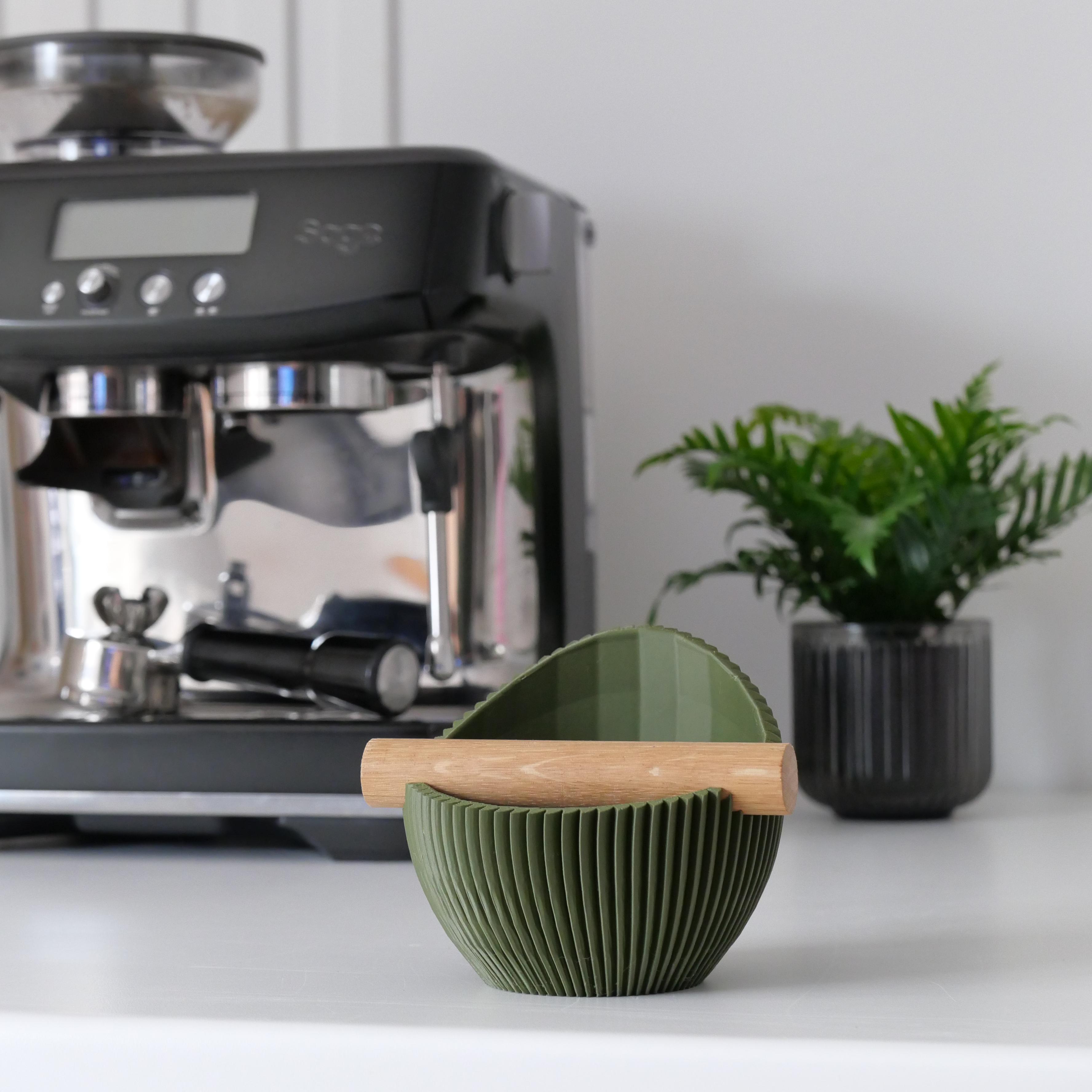 Green pleated knock box on a white surface with a coffee machine in the background