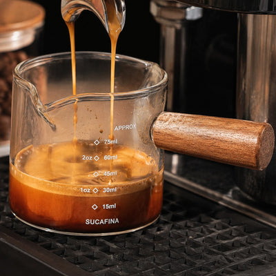 Espresso pouring into 100ml glass measuring cup under coffee machine