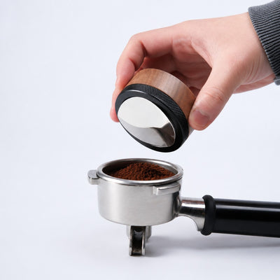 Hand using walnut espresso distribution tool to level coffee grounds in a portafilter