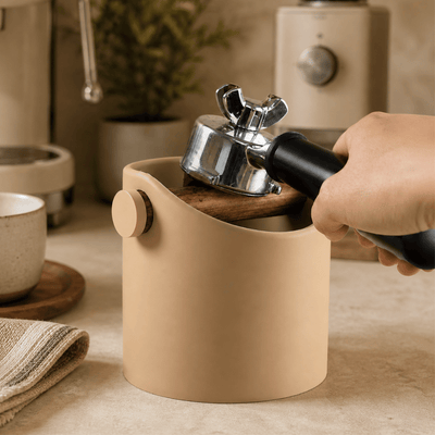 Striking a portafilter against the real oak bar of a cylindrical minimalist espresso knock box to empty coffee pucks.