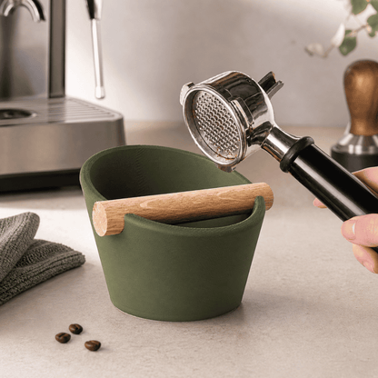 Hand knocking a portafilter against the real oak wood bar of an olive green matte espresso knock box.