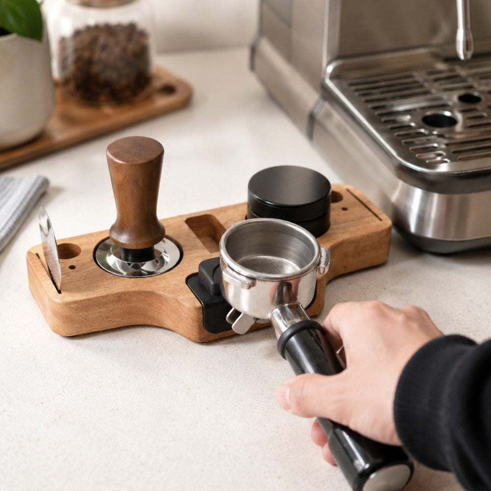 Person using a manual coffee press on a wooden tray with coffee-making equipment in the background.
