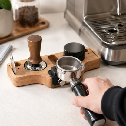 Person using a manual coffee press on a wooden tray with coffee-making equipment in the background.