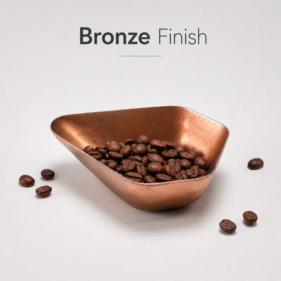 Bronze bowl filled with coffee beans on a light gray background