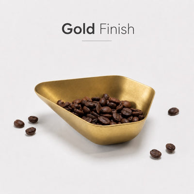 Gold triangular bowl filled with coffee beans on a light gray background