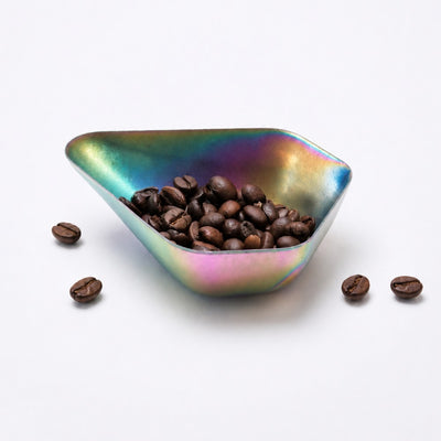 Triangular stainless steel dish filled with coffee beans on a white background