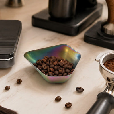 Colorful bowl filled with coffee beans on a marble surface with coffee-making equipment.