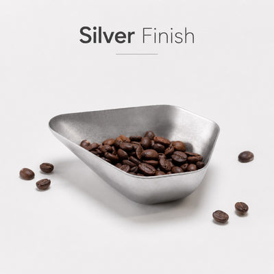 Triangular silver bowl filled with coffee beans on a light gray background