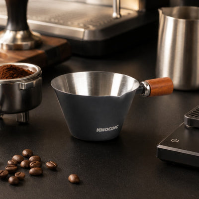 Espresso measuring cup beside coffee machine and barista tools
