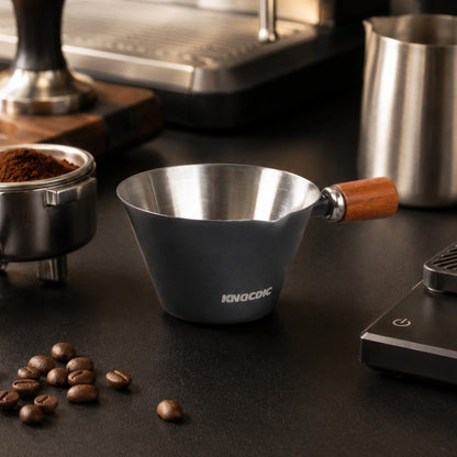 Espresso measuring cup beside coffee machine and barista tools