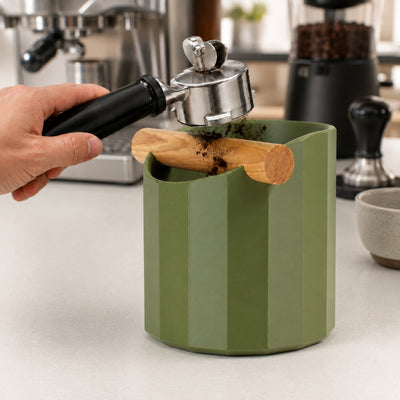 Rapping an espresso portafilter against the real hardwood bar of a modern geometric coffee waste bin.