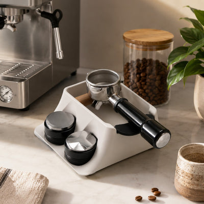 Modern minimalist kitchen counter featuring the white KNOCDIC espresso tamping station next to a coffee machine.