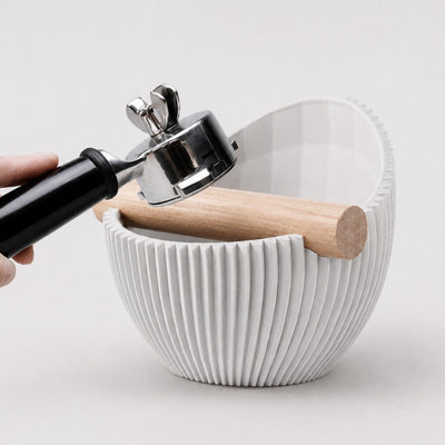 Using an espresso portafilter to knock out a spent coffee puck into a white textured Nova knock box.