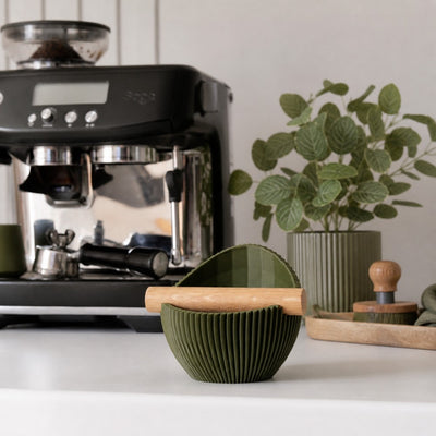 A textured olive green compact espresso knock box placed perfectly on a home barista coffee bar station.