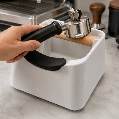 An espresso portafilter resting perfectly level inside the black carbon fibre handle stabilizer cradle for a tamping demonstration.