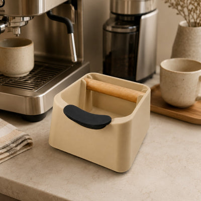 Desert Tan knock box with black handle on a kitchen counter with coffee-making equipment in the background.