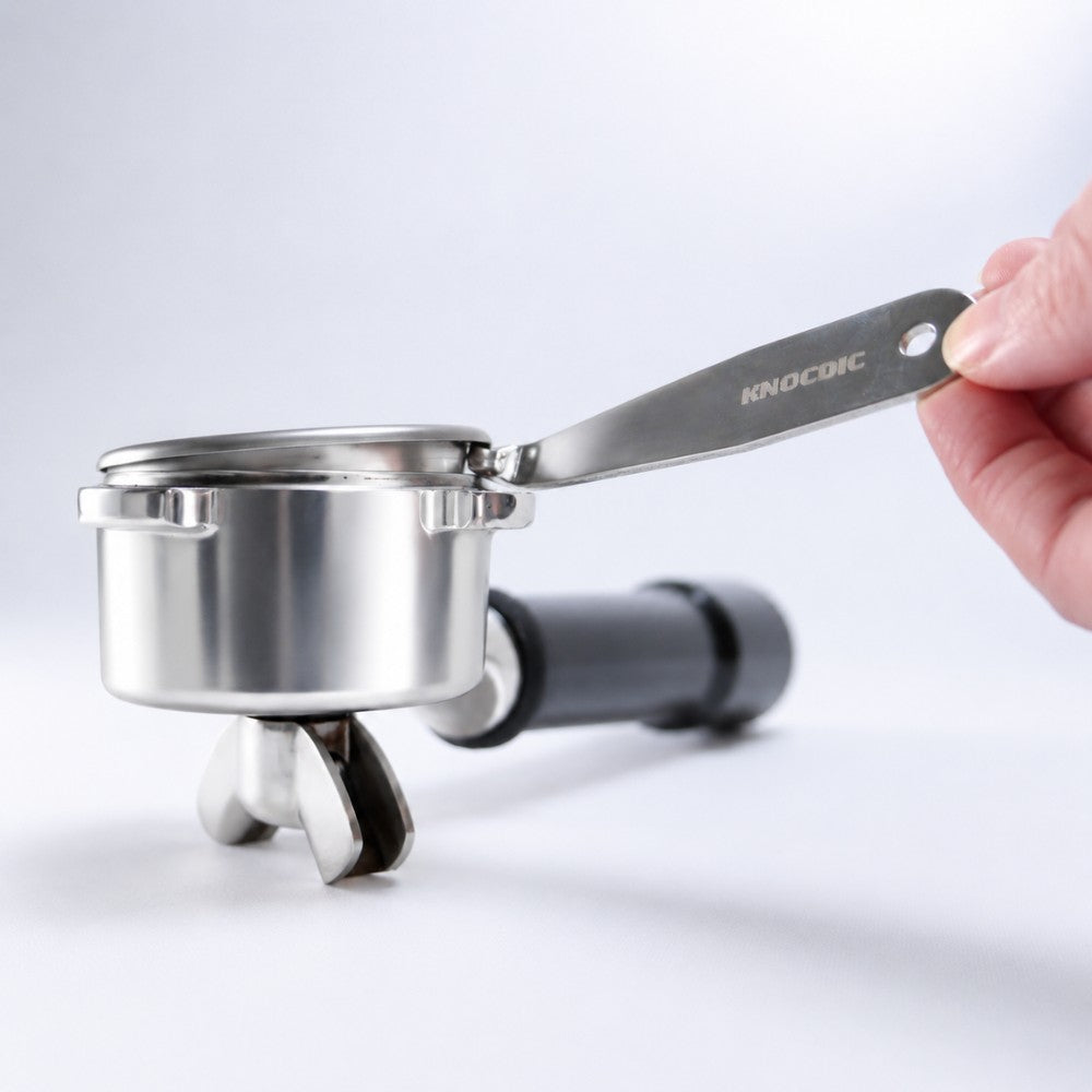Hand holding a stainless steel espresso basket remover on a white background