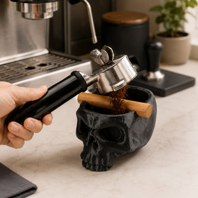 Tapping a portafilter against the wood bar of a black skull coffee waste bin to empty an espresso puck.