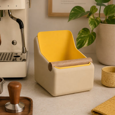 A pastel yellow curved square coffee knock box styled neatly alongside a high-end home espresso machine grinder setup.