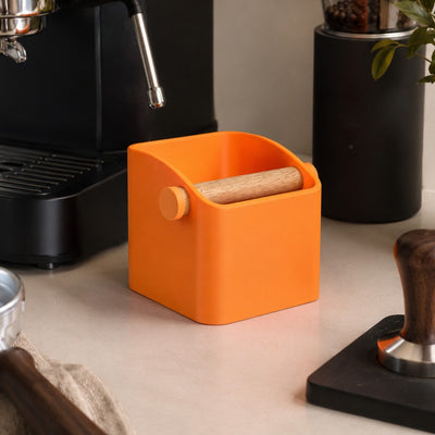 Orange coffee container with wooden scoop on a kitchen counter next to a black espresso machine.