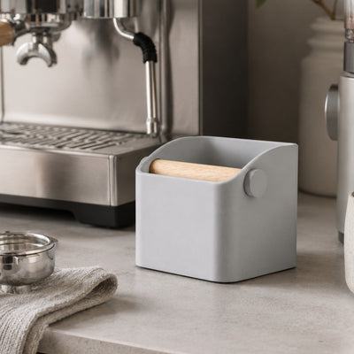 Gray container with a wooden block on a kitchen counter next to an espresso machine.